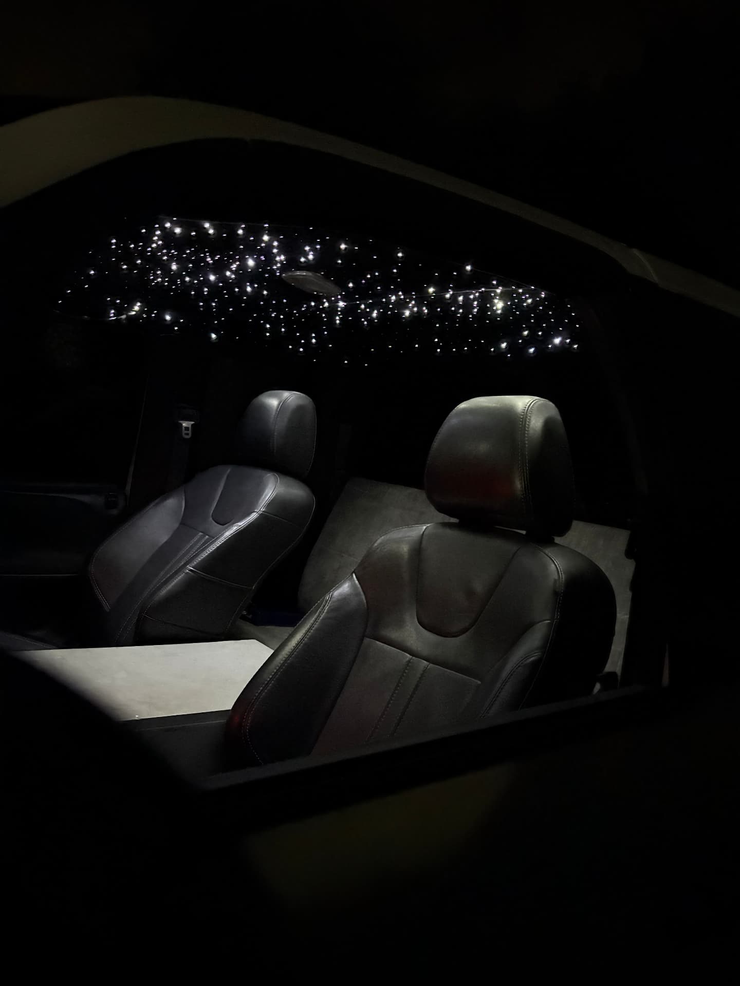 Night view of a car cabin with bright white fiber-optic stars across a dark headliner and black leather seats
